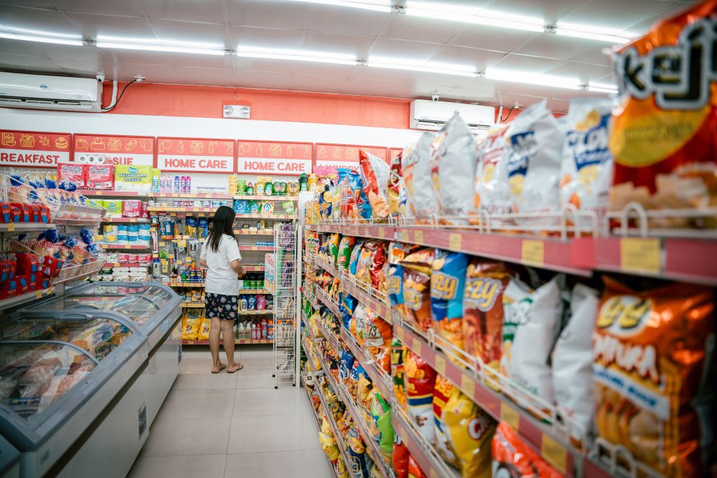 食品製造商風險管控:如何防範過期品流入黑市 A woman browsing snack shelves at a supermarket, surrounded by various chips packages.